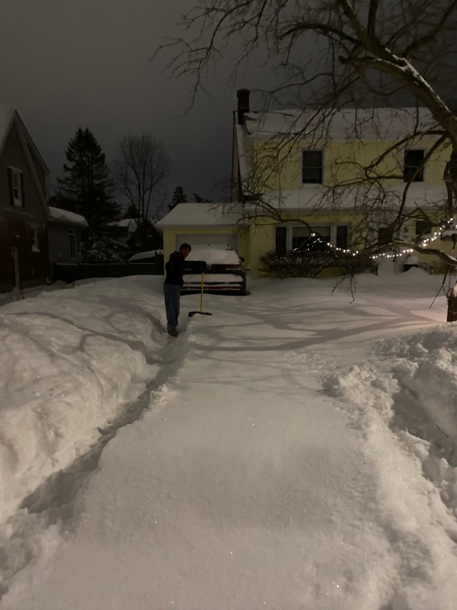 A long driveway under untouched snow, with one narrow strip just shovelled beside a car.