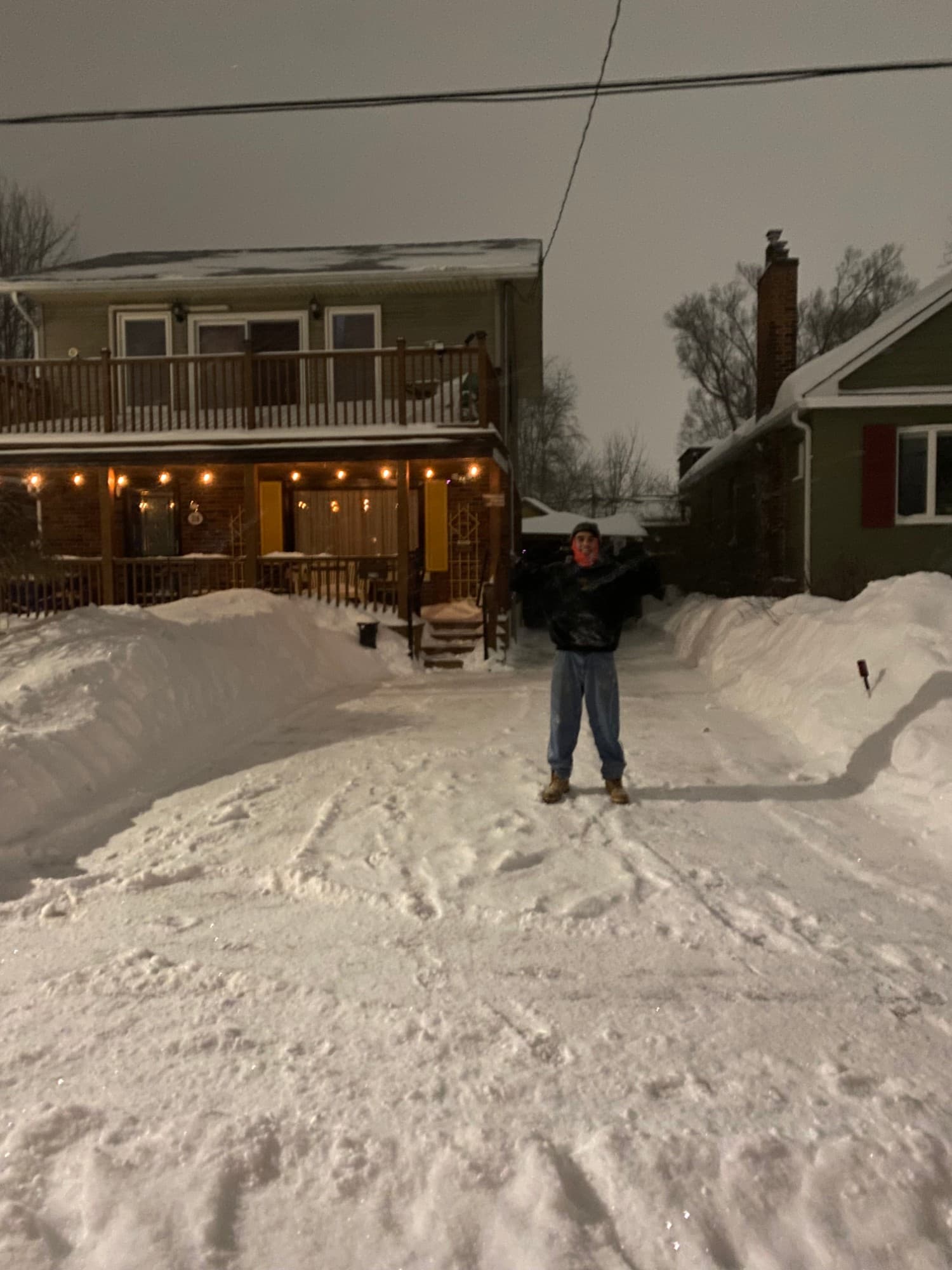 The same house and driveway, cleared down to a packed surface with tall snowbanks on both sides.